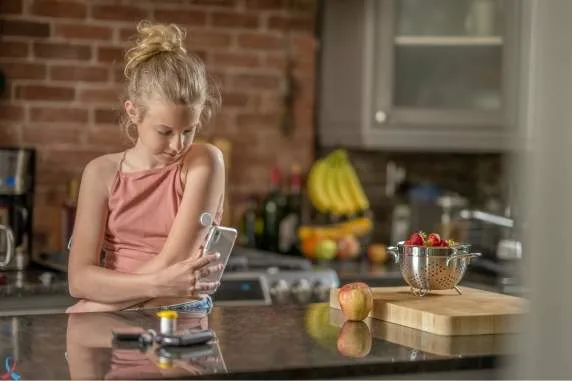 A girl using her phone in the kitchen.